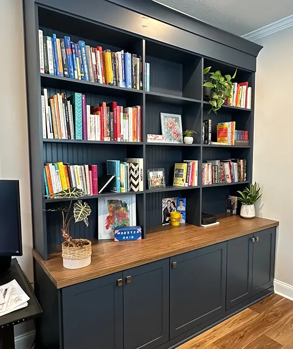 Custom-built dark navy bookcase with a wood countertop and lower cabinets. The shelves are filled with colorful books