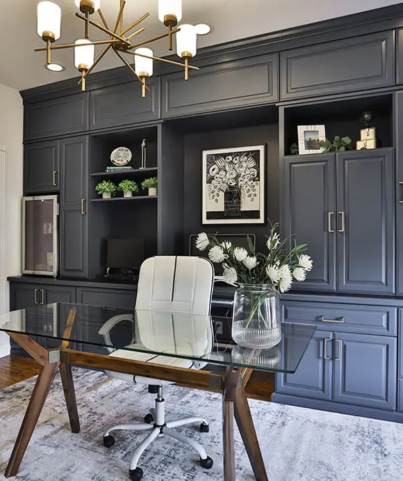 Sophisticated home office featuring dark built-in cabinetry with gold hardware, open shelving with decor, and a glass-top desk paired with a white ergonomic chair