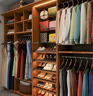 Custom walk-in closet with warm wood cabinetry, featuring organized clothing racks, open shelves with handbags, and illuminated shoe storage