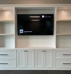 Built-in white entertainment center with a mounted flat-screen TV, flanked by open shelving and lower cabinets