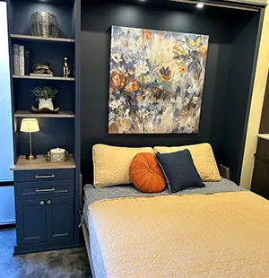 Built-in Murphy bed with navy blue cabinetry, integrated shelves and drawers, and a cozy bed dressed in neutral bedding
