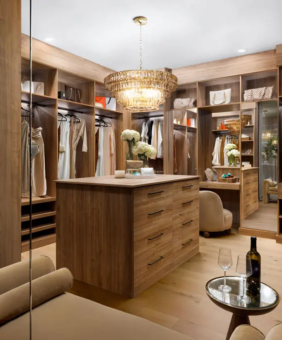 Large walk-in closet featuring custom wood-grain cabinetry, a center island with drawers, a crystal chandelier, and integrated boutique lighting.