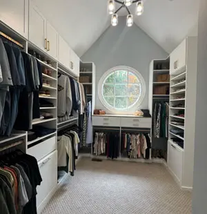 Custom walk-in closet with white cabinetry, double hanging sections, open shelving, drawers, and a large arched window providing natural light.