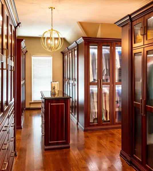 Long walk-through wardrobe with wood cabinets, glass doors, and a narrow center island.