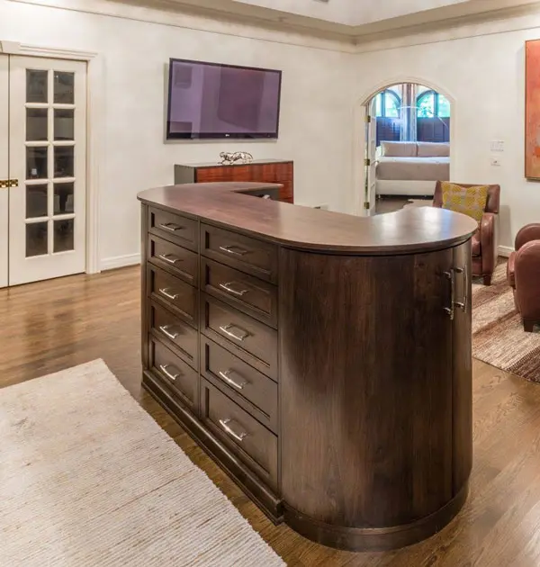 Curved wood storage island with multiple drawers placed in the center of a room.