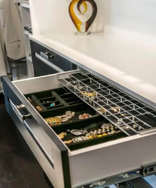 Custom double-deck jewelry drawer with lucite inserts and velvet lining, showcasing organized rings and necklaces in a modern black and white walk-in closet island.