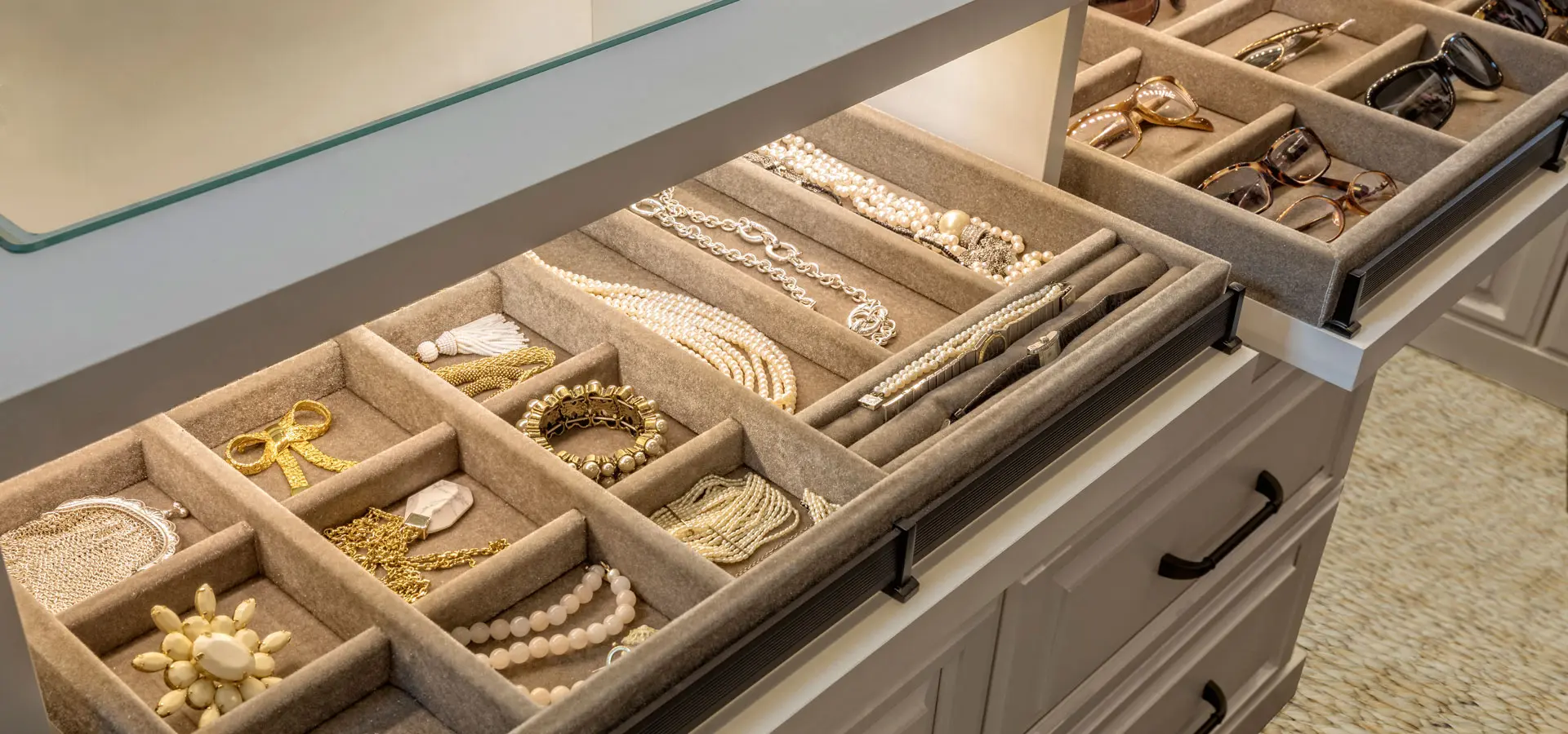 Close-up of a custom velvet-lined jewelry drawer and a separate sunglass organizer inside a white closet island.