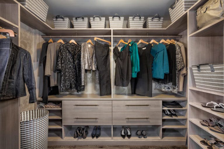 A custom closet with hanging clothes and shoe shelves