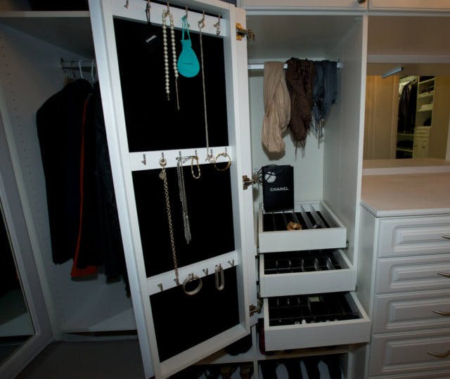 A jewelry rack with storage shelves inside and hooks on the inside of the door