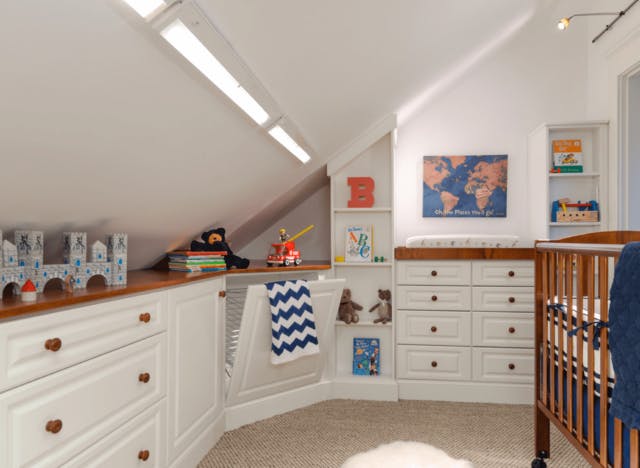 A kids room with a changing table, crib, and hidden laundry hamper