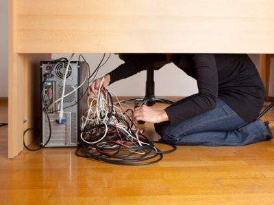 person tieing up cords under desk