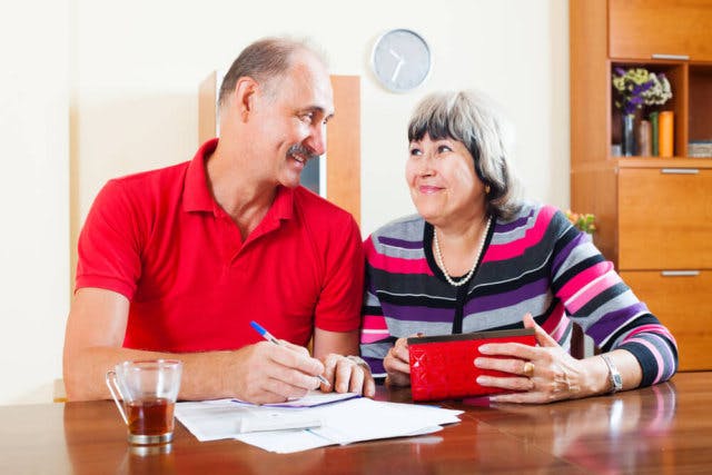 An older couple smiling while writing checks