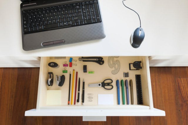 An open drawer desk filled with writing supplies. A laptop and mouse sit on the desk