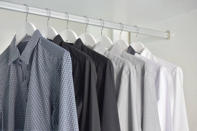 a number of men's collared shirts hang in a plain white closet