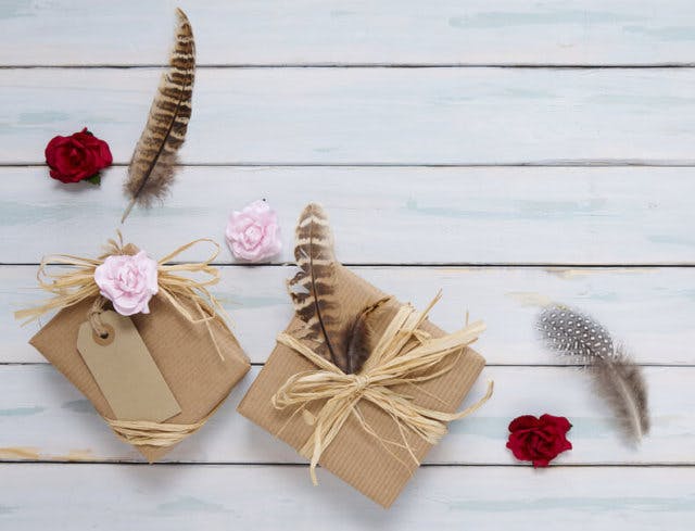 Two paper wrapped packages sit on a white-washed table alongside feathers and roses