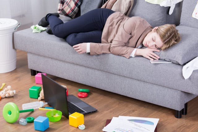 A woman asleep on a couch. She is surrounded by a laptop and children's toys
