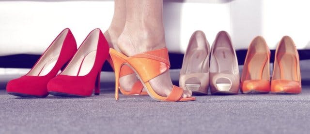 A woman standing in orange heels. She has three other pairs near her feet