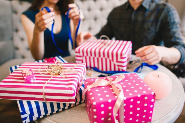 A man and woman open presents wrapped in pink and blue stripes
