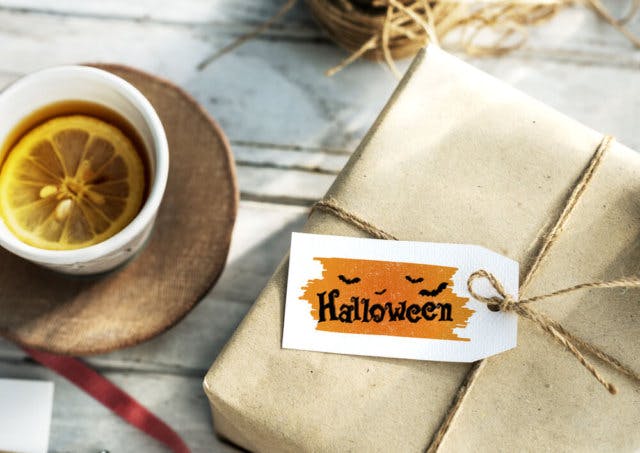 A gift wrapped in plain paper and twine with a label saying "Halloween." A mug of tea with a lemon slice sits beside it.