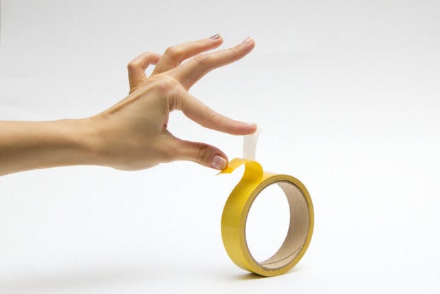 A hand separates a protective film from a strip of tape