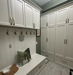Elegant mudroom with built-in white cabinetry, brass hooks, and a cushioned bench