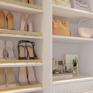 Gold-accented shoe fences and open shelving create a boutique-style display for heels, handbags, and personal touches in this elegant custom closet vignette.