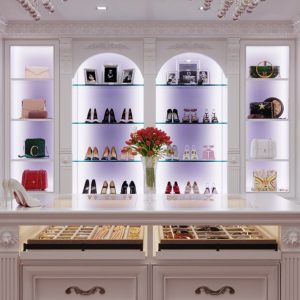 White closet with arched illuminated display shelves, with LED lighting for showcasing shoes and bags. Centered around a double-sided island with velvet-lined jewelry drawers.