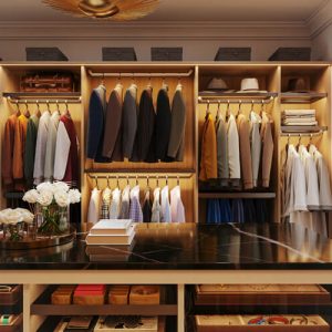 Masculine closet with amber lighting, black marble countertop on the island, two-tier hanging rods for suits and shirts, and top-shelf hat and luggage storage