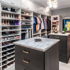 Modern custom closet with dual islands, extensive shoe storage, hanging sections for men’s and women’s clothing, and display shelves for accessories.