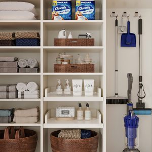 Organized linen and utility closet featuring rolled towels, labeled baskets, and mounted cleaning supplies with vacuum storage.
