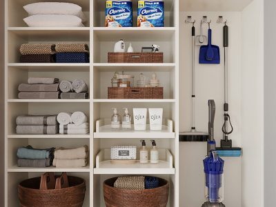Organized linen and utility closet featuring rolled towels, labeled baskets, and mounted cleaning supplies with vacuum storage.