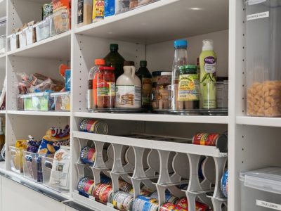 Custom pantry with labeled clear bins, rotating trays, and a can dispenser for organized food and drink storage.