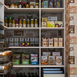 Walk-in pantry featuring retro café wallpaper, fully stocked open shelving, and sliding racks for spices and snacks.