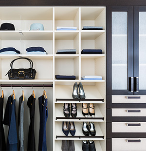 Custom closet system with open cubbies for hats and folded clothing, hanging space for jackets and pants, shelves for shoes, and a set of sleek drawers with frosted glass cabinet doors
