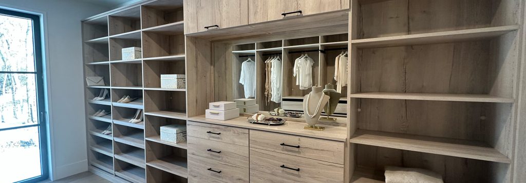 Spacious walk-in closet with light wood built-ins, open shelving, and a central vanity area featuring a mirror, jewelry display, and elegant organization