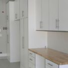 Custom garage storage with white cabinets, upper storage, drawers, and a butcher block countertop workspace in a modern garage.
