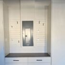 Custom white garage storage system with tall cabinets, drawers, countertop workspace, and accessible electrical panel storage integration.