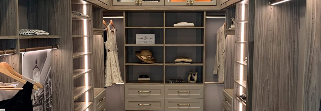 Walk-in closet with custom woodgrain cabinetry, LED-lit hanging rods, and open shelving; features a center section with drawers, display shelves