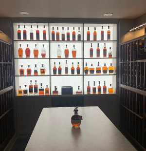 Backlit liquor display featuring an organized collection of whiskey bottles, framed by dark wood wine racks on either side and a central marble-topped island