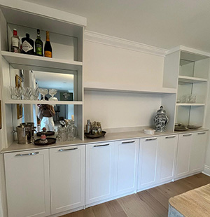 Built-in white cabinetry with open shelving and mirrored back panels, used for displaying glassware, spirits, and decorative items in a modern home bar or dining room area