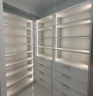 Minimalist walk-in closet with light wood cabinetry, built-in drawers, and open shelving, all illuminated by sleek vertical LED lighting