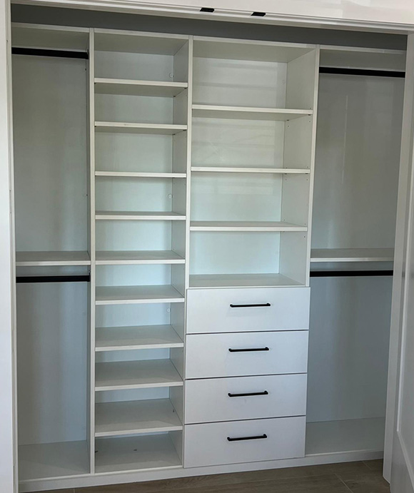 Modern white built-in closet with open shelving, four drawers with black handles, and multiple hanging rods for versatile clothing storage