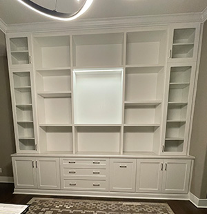 Custom built-in wall unit with white cabinetry, open shelving, and lower drawers, designed for a living or media room. The center features a framed section ideal for a television or artwork