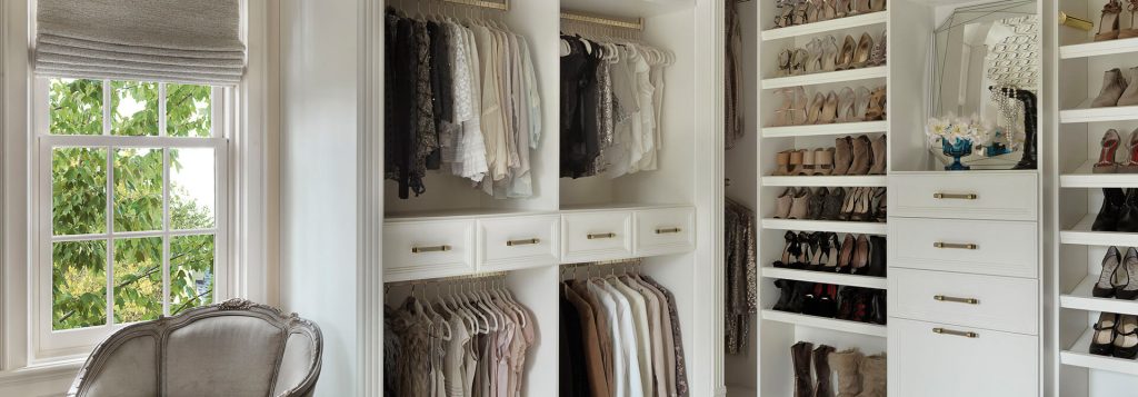 Elegant walk-in closet featuring white built-in cabinetry with gold handles, open hanging sections for clothing, multiple shoe shelves
