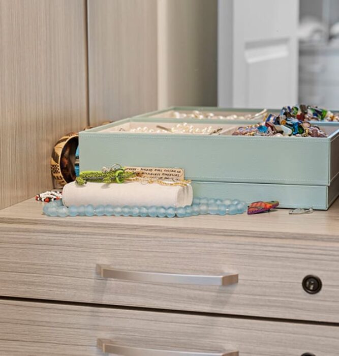Jewelry box with assorted bracelets, pearls, and necklaces displayed on a built-in closet drawer surface.