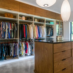 Walk-in closet with floor-to-ceiling wood paneling, black glass cabinetry, and LED-lit shelving
