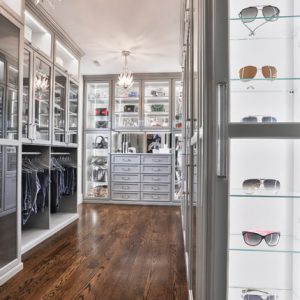 Custom walk-in with floor-to-ceiling mirrors, velvet-lined drawers, and a backlit glass display case showcasing sunglasses and accessories.