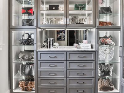 Modern gray closet with integrated lighting, glass display shelves for designer handbags, and a dedicated vanity station with full-extension drawers.