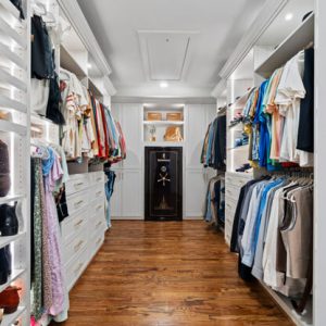 Classic closet with white cabinetry, black accent drawers, wood floors, and built-in wall safe