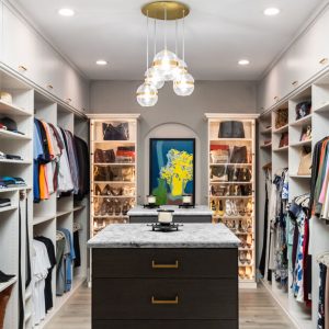 Walk-in with dual islands, extensive hanging and shoe space, and accent-lit shelves highlighting handbags and accessories.